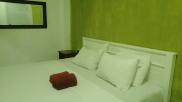 Una cama con ropa de cama y almohadas blancas, una toalla roja, una mesita de noche y un espejo en la pared.