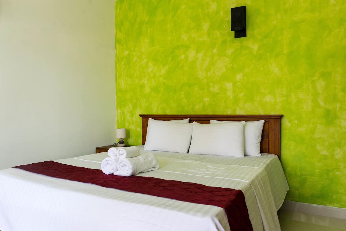 A neatly made bed with white linens and a red blanket, a wooden headboard, and a green wall with a black switch.