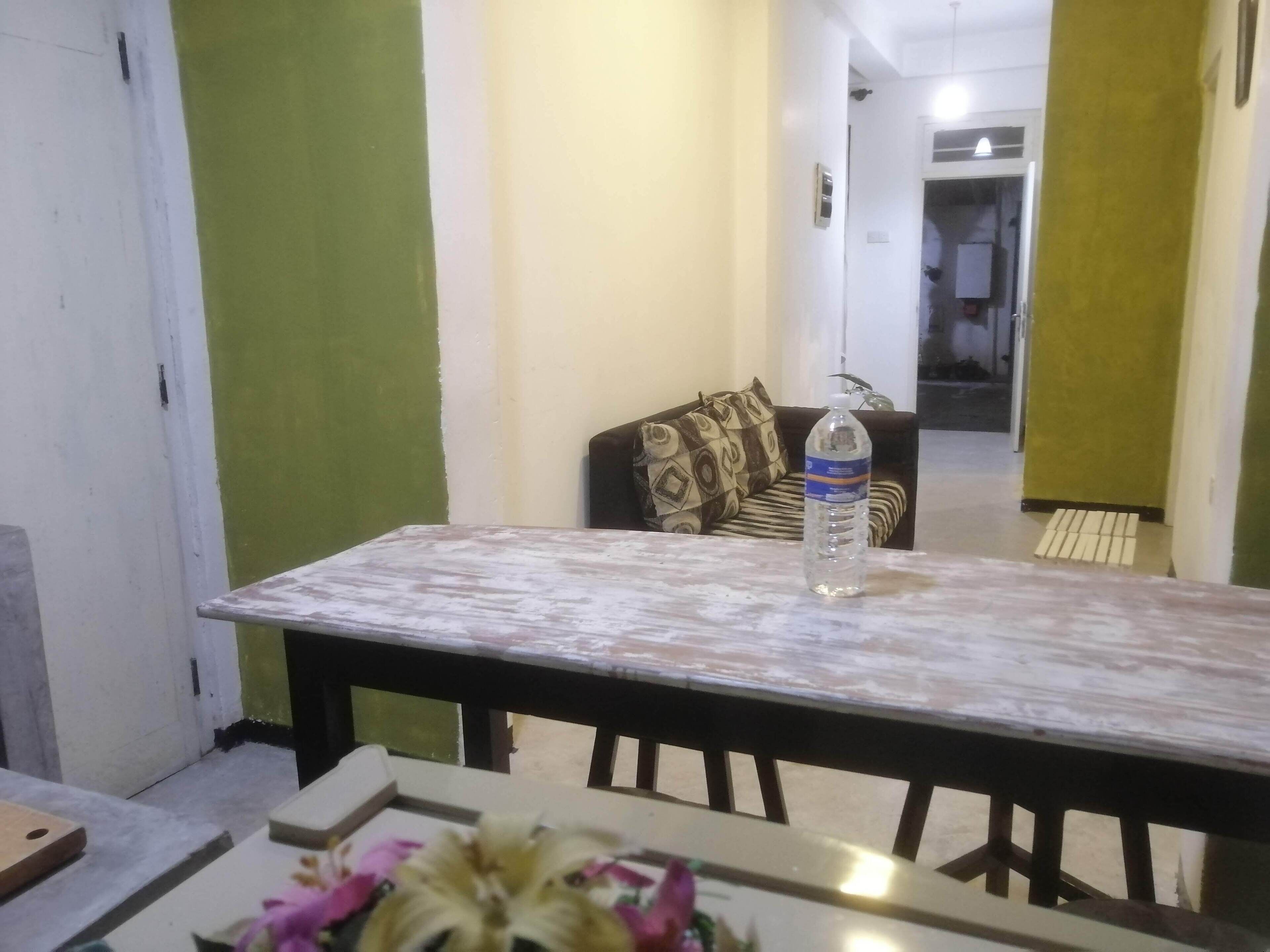 A dining area with a table and chairs, a sofa in the background, and a water bottle on the table.