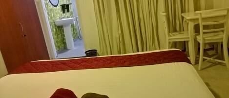 Une chambre d’hôtel avec un lit, une serviette rouge et marron, une chaise blanche, un lavabo et un miroir.