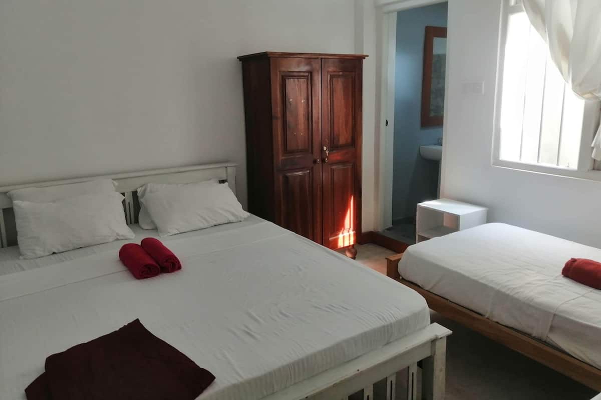 A hotel room with two beds, a wooden wardrobe, a bathroom with a sink, and a window with curtains.