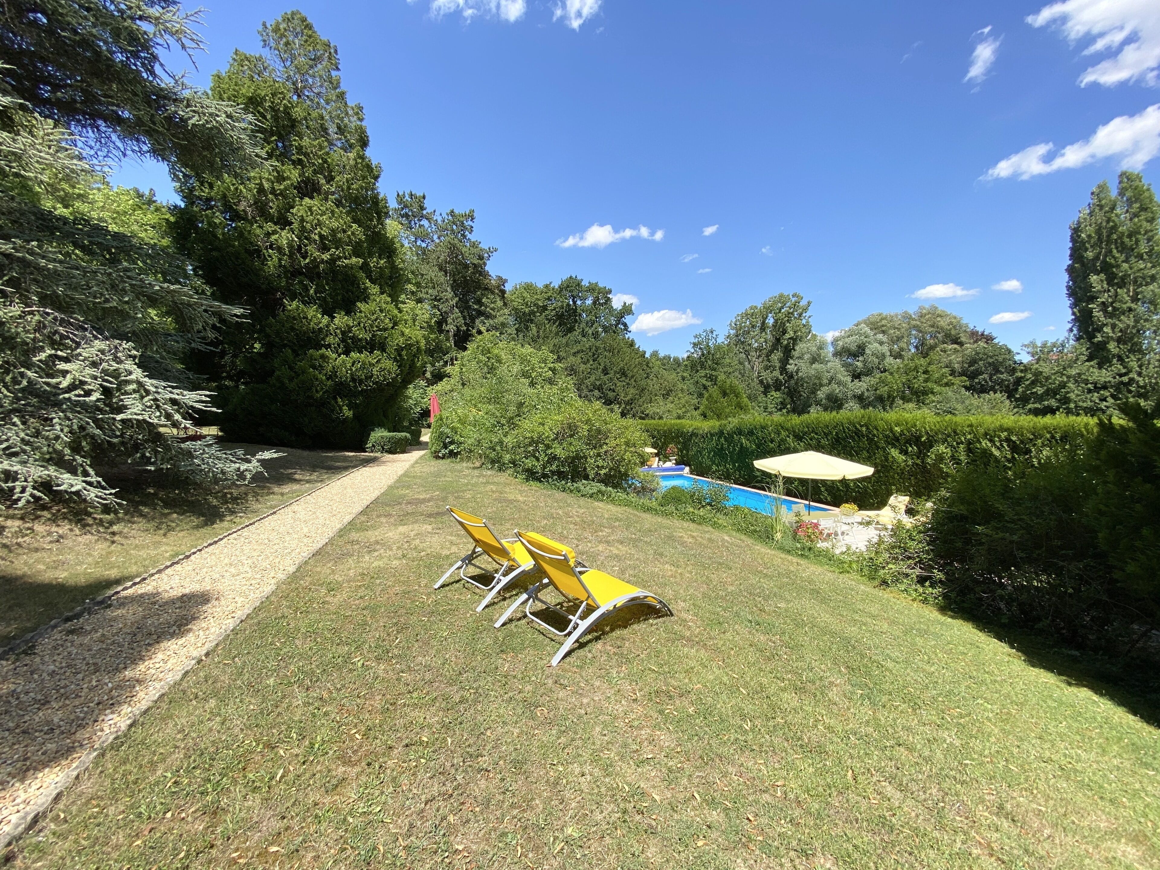 A backyard with a swimming pool, a paved path, and yellow chairs.