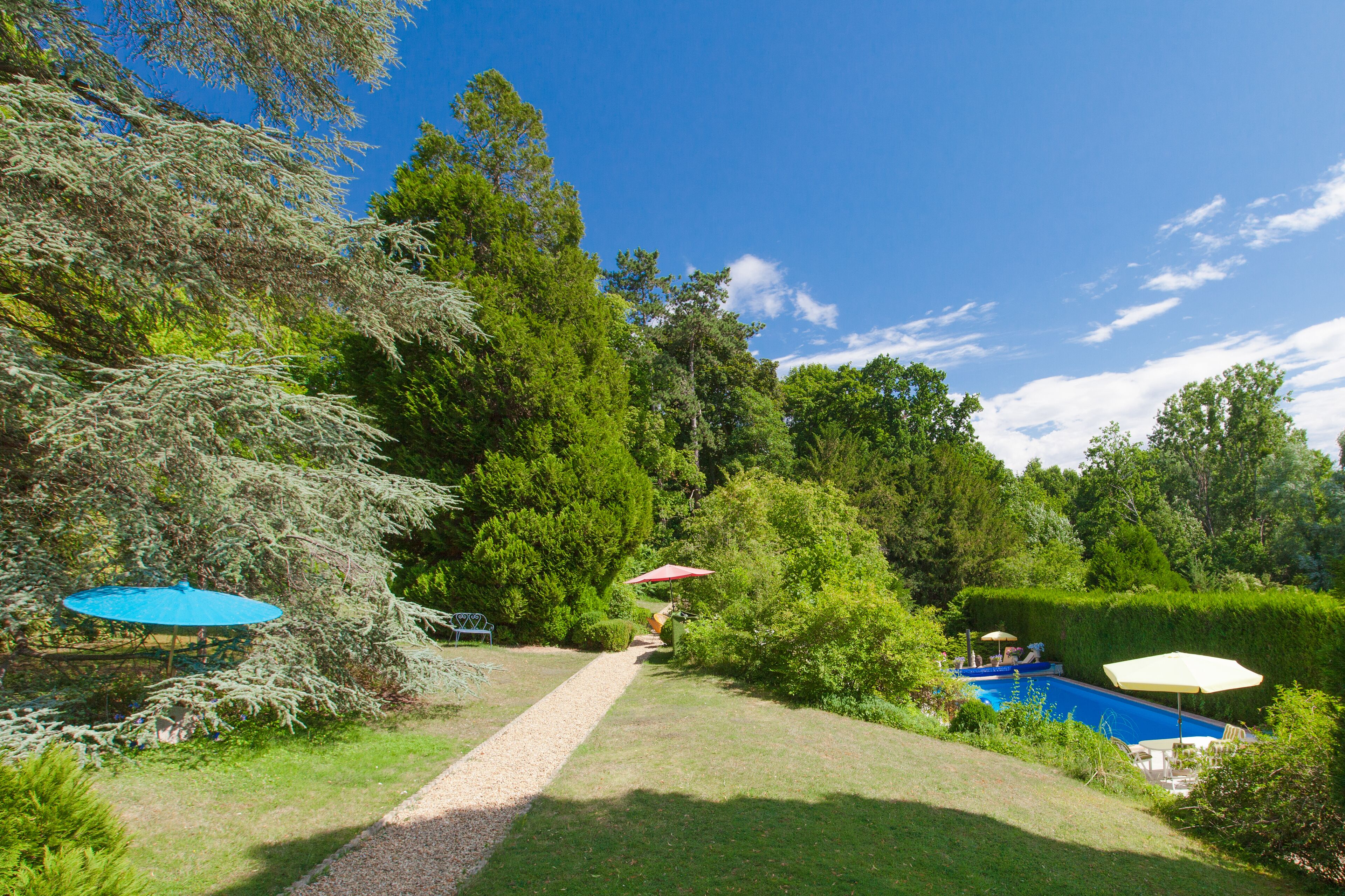 Un patio trasero con piscina, un sendero y mobiliario de exterior.