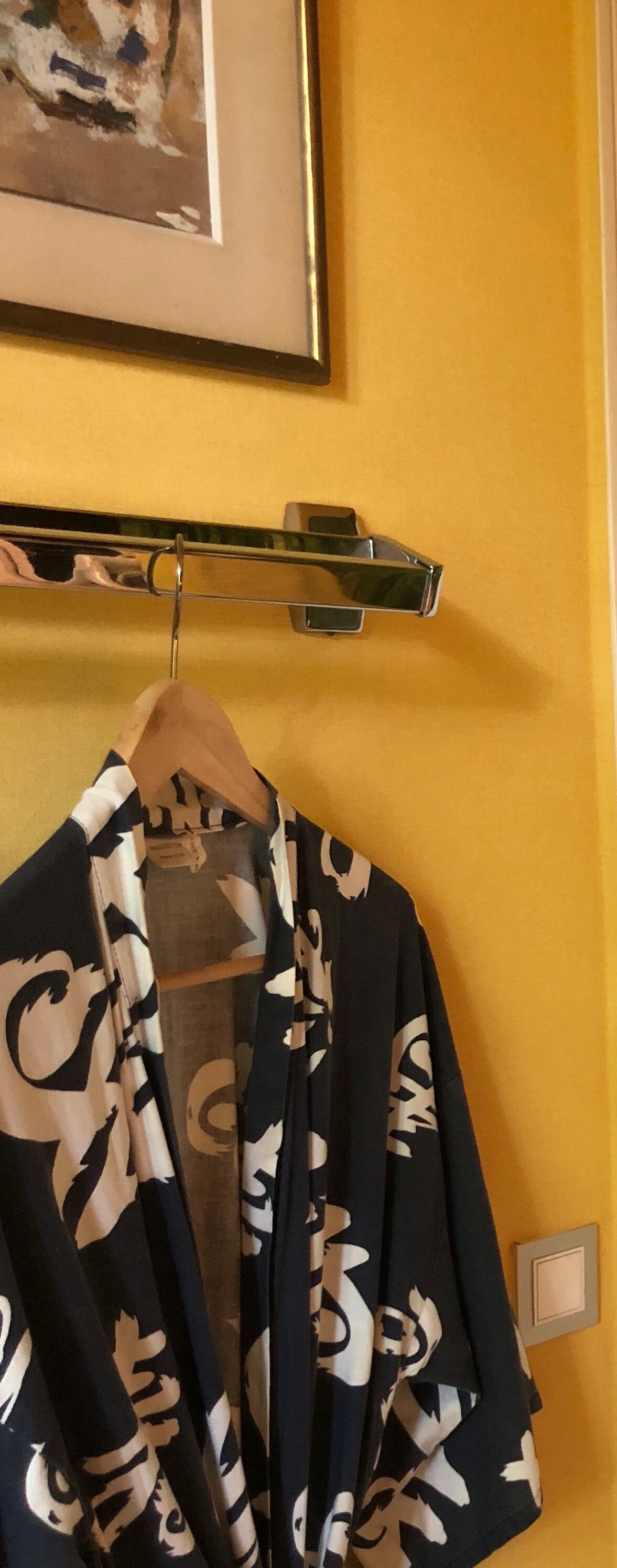 Una habitación con pared amarilla, un cuadro enmarcado y un perchero con una prenda.