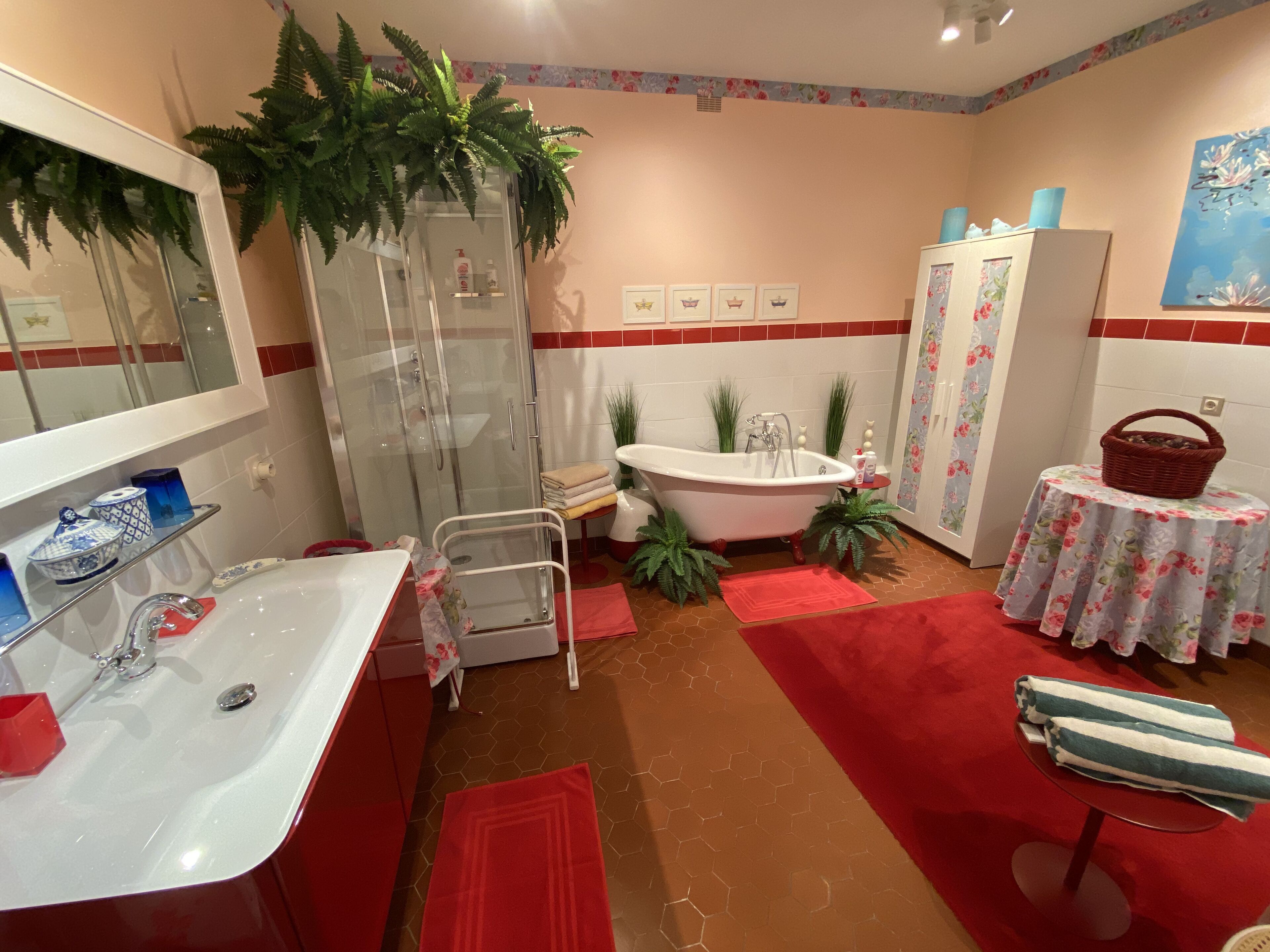 A bathroom with a glass-enclosed shower, a white sink, a bathtub, and a small round table with a floral tablecloth.