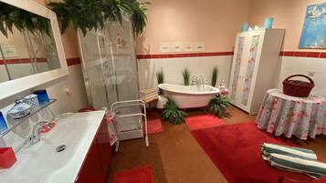 A bathroom with a glass-enclosed shower, a white sink, a bathtub, and a small round table with a floral tablecloth.