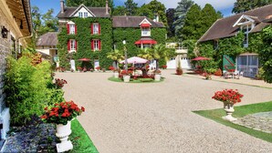 A courtyard with a gravel path, a central seating area with tables and chairs, and a building with ivy-covered walls and red shutters. - Manoir des Cavaliers - BnB (Vineuil-Saint-Firmin)