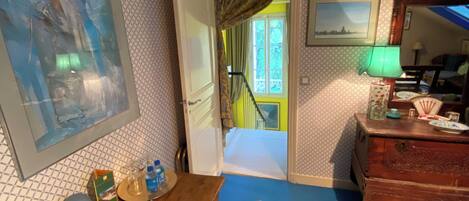 Una habitación con un escritorio de madera, una silla y una alfombra azul. Se ve una escalera que sube a un balcón con barandilla amarilla.