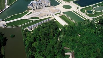 Vista aérea de una extensa propiedad histórica con jardines formales, un edificio central y un lago.