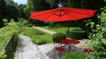 A stone pathway leading to a red umbrella table and chairs in a garden setting.