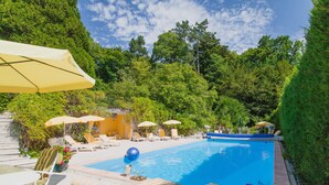 A pool area with lounge chairs and umbrellas, surrounded by lush greenery. - Manoir des Cavaliers - BnB (Vineuil-Saint-Firmin)