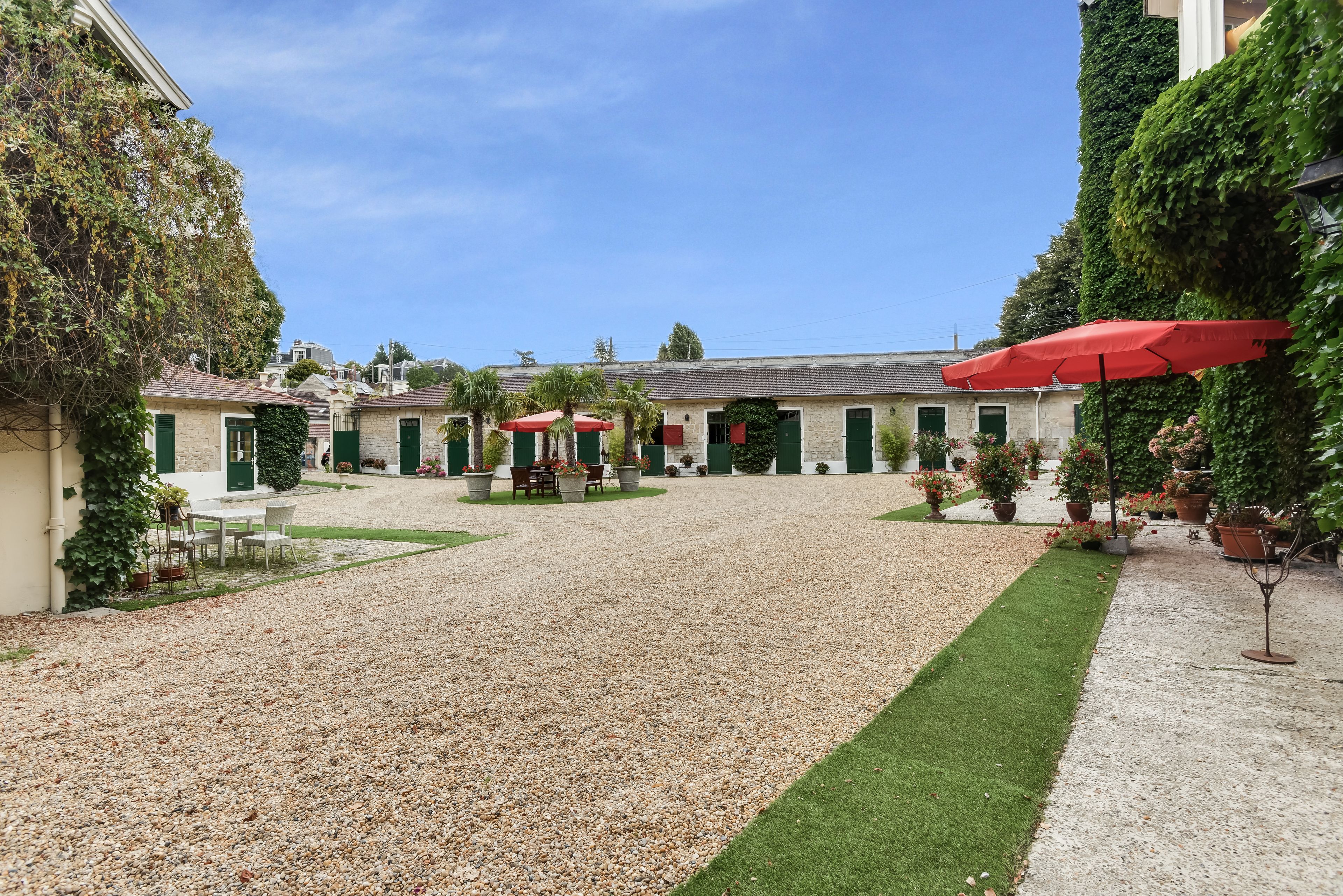 A courtyard with a gravel path, green lawn, outdoor seating, and red umbrellas.