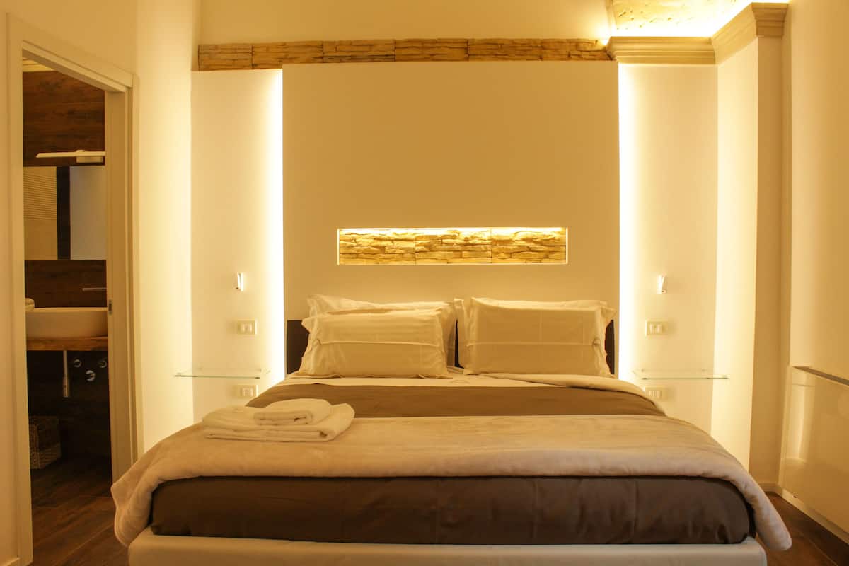 A neatly made bed with a headboard, bedside tables, and a wall-mounted light fixture.