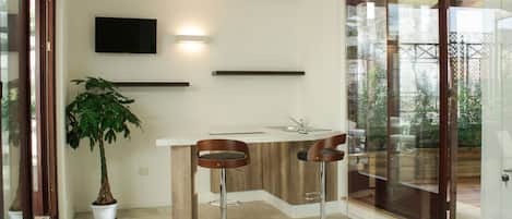 A modern kitchen with a built-in island, two bar stools, a potted plant, and a flat-screen TV mounted on the wall.