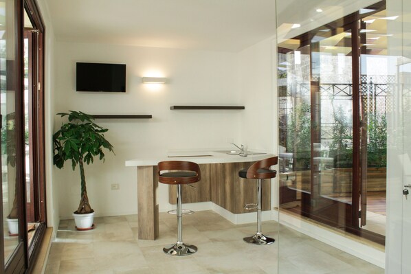 A modern kitchen with a built-in island, two bar stools, a potted plant, and a flat-screen TV mounted on the wall. - Signuria Dimora Esclusiva (Lecce)