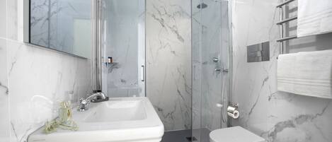 Un baño moderno con cabina de ducha de vidrio, un lavabo blanco, un bidé y un pared revestida de mármol.