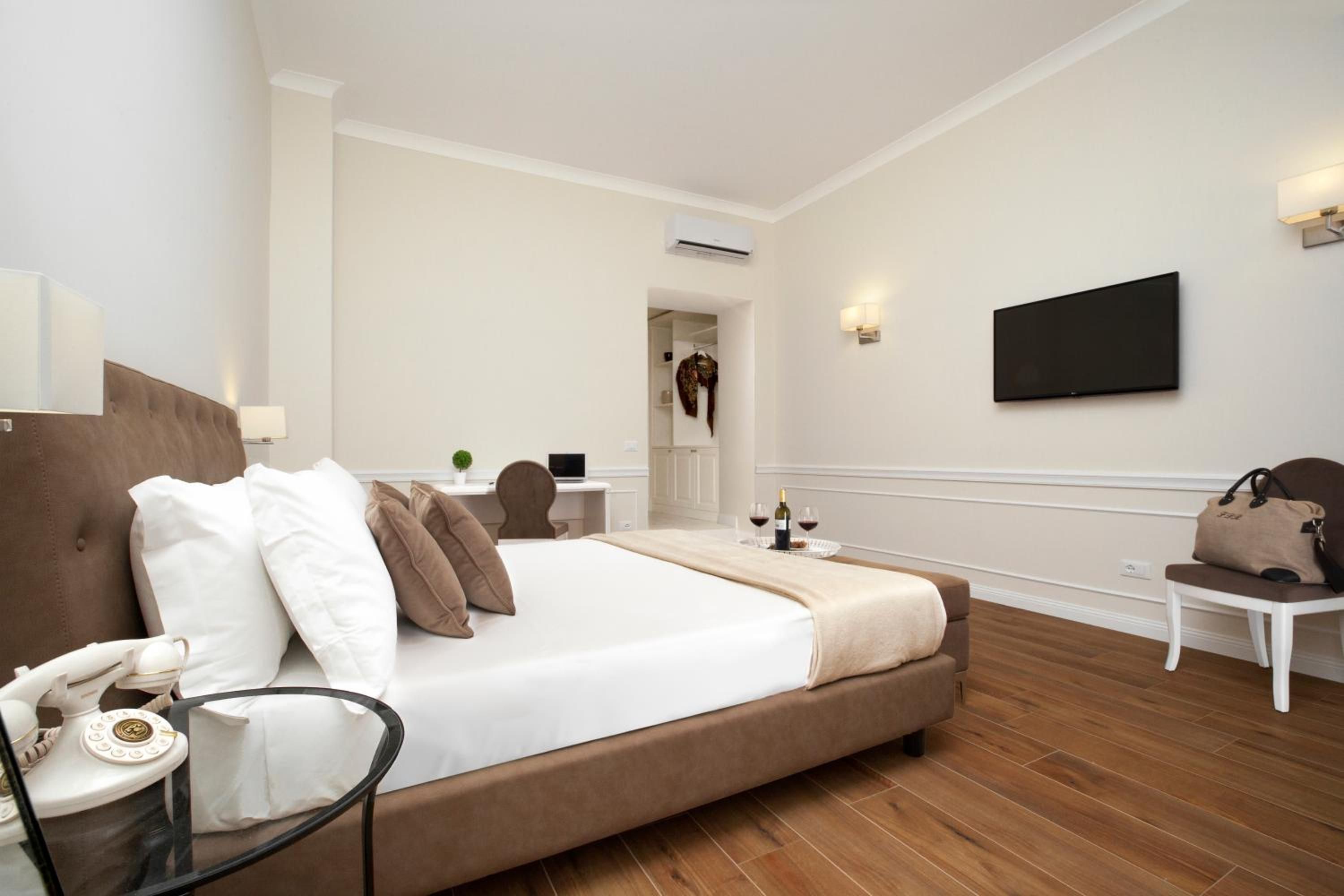 Ein Hotelzimmer mit einem großen Bett, einem Schreibtisch, einem Sessel, einem Flachbildfernseher und einem Telefon.