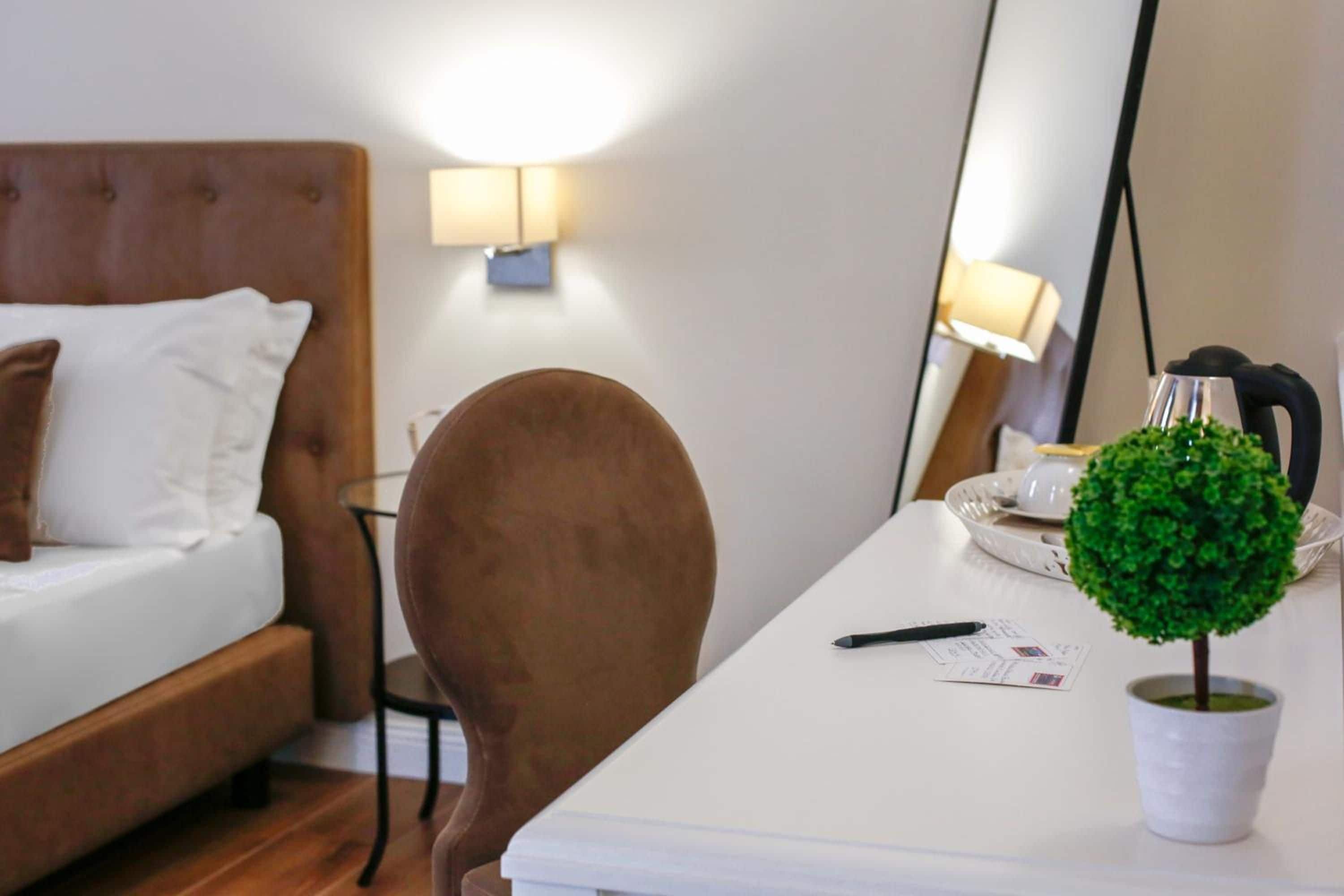 Une chambre d’hôtel équipée d’un lit, d’un bureau, d’une chaise, d’une lampe, d’une plante en pot et d’une bouilloire.