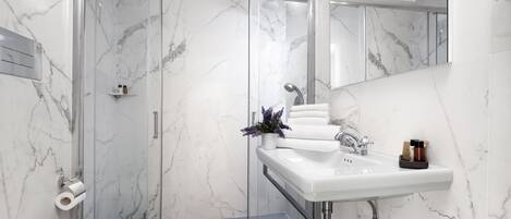 Un baño moderno con cabina de ducha de vidrio, un lavabo blanco y pared revestida de mármol.