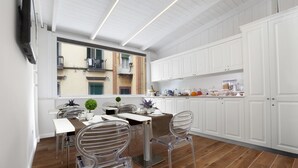 A modern kitchen with white cabinets, a dining area with clear chairs, and a view of a building through a large window. - La Fontanina Suites (Naples)
