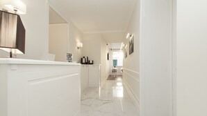 A hallway with a marble floor, white walls, and a reception desk with a lamp. - La Fontanina Suites (Naples)