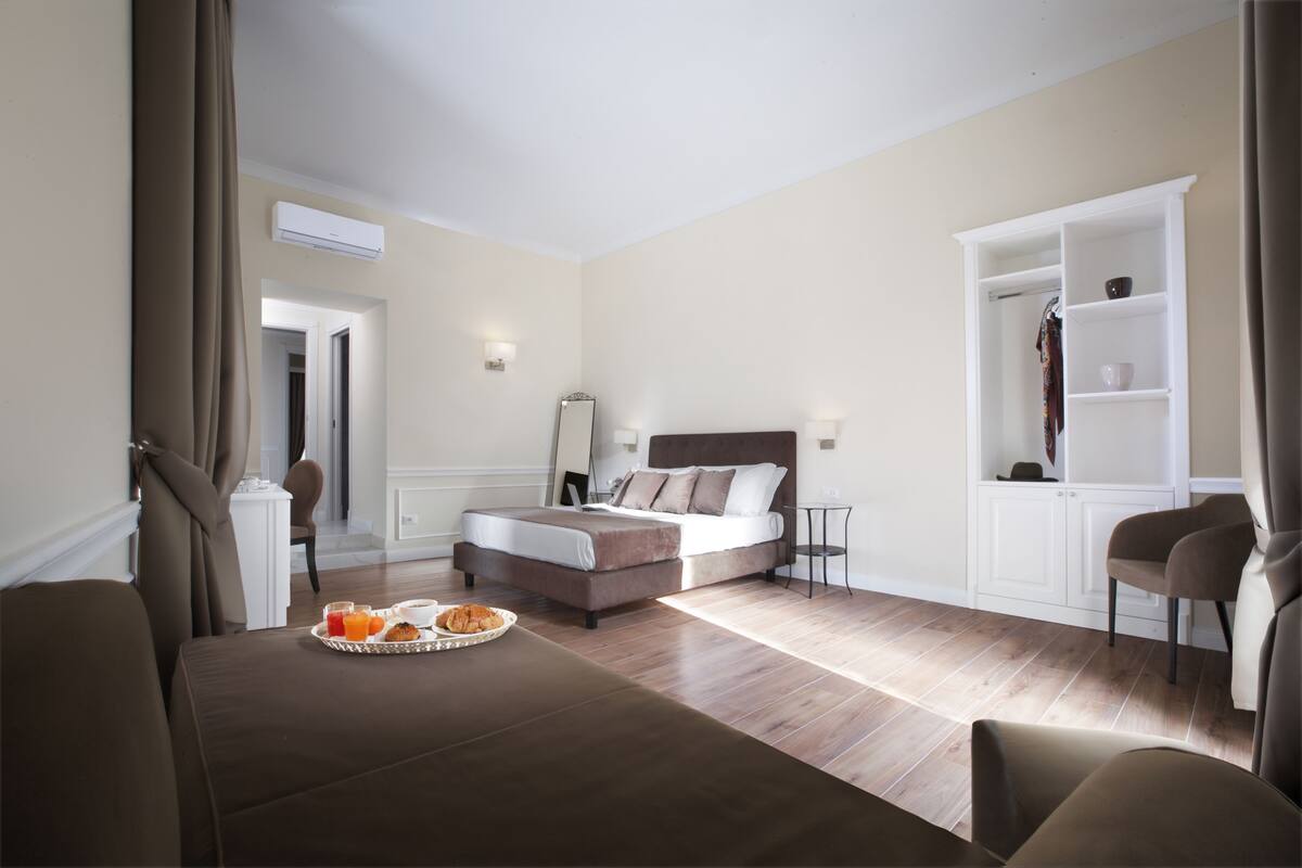 A modern hotel room with a bed, a dining table with breakfast, a wardrobe, and a mirror.