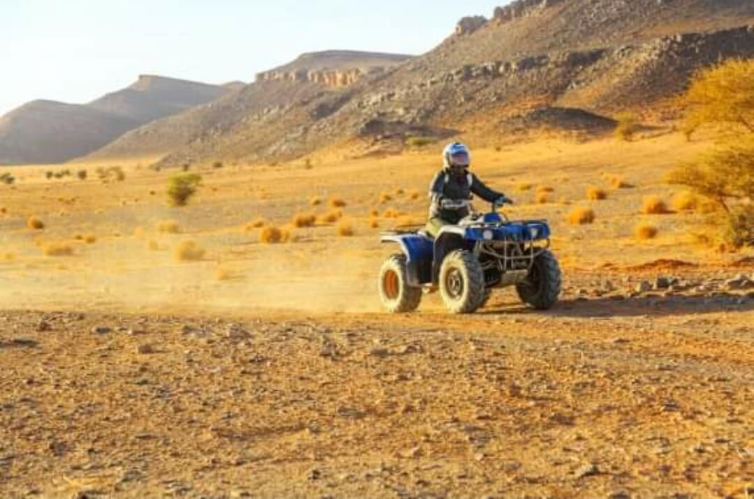 A person riding an ATV on a dirt road with rocky terrain and sparse vegetation.