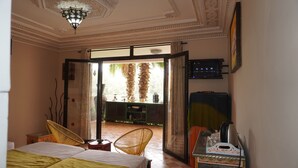 A room with a bed, two chairs, a TV, and a view of palm trees through an open door. - Riad Saida Atlas (Lalla Takarkoust)