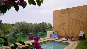 A pool area with a mural of palm trees, lounge chairs, and a green fence. - Riad Saida Atlas (Lalla Takarkoust)