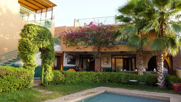A courtyard with a swimming pool, lush greenery, and a building with a balcony. - Riad Saida Atlas (Lalla Takarkoust)