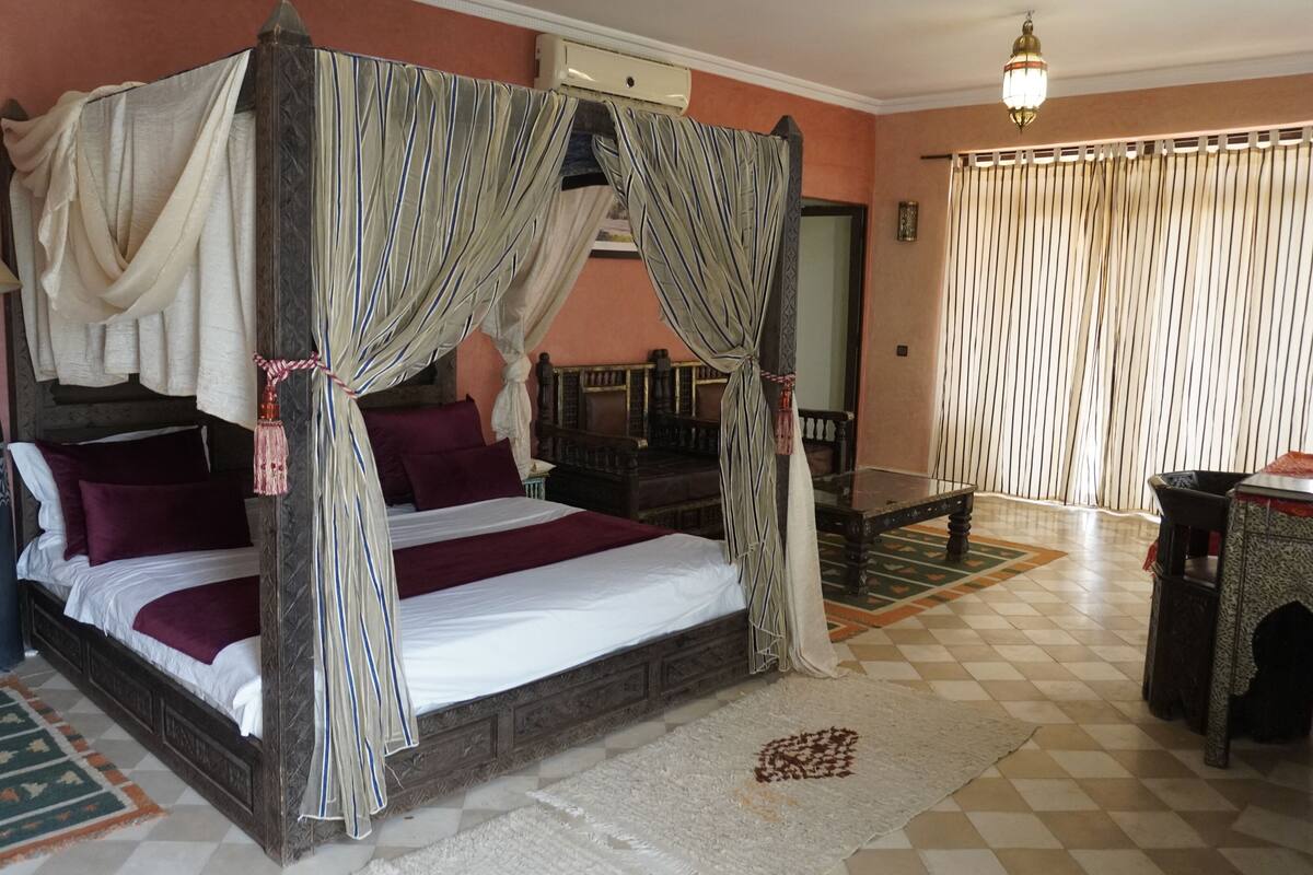 A four-poster canopy bed with a checkered floor, a standing lamp, and a patterned rug.