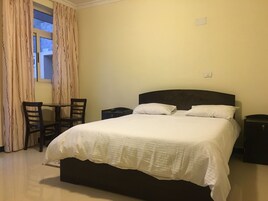 Un dormitorio con una cama grande, dos mesitas de noche, una pequeña mesa con sillas y una ventana con cortinas.