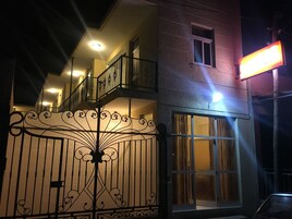 Un edificio con balcón, entrada protegida por una reja y un cartel iluminado.