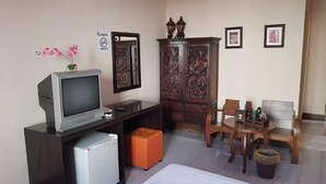 Una habitación compacta con televisión, un refrigerador pequeño, un armario de madera, una mesa de comedor con sillas y un cesto de basura.