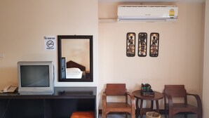 Habitación de hotel con televisor, espejo, cartel de no fumar, aire acondicionado y tres adornos en la pared.