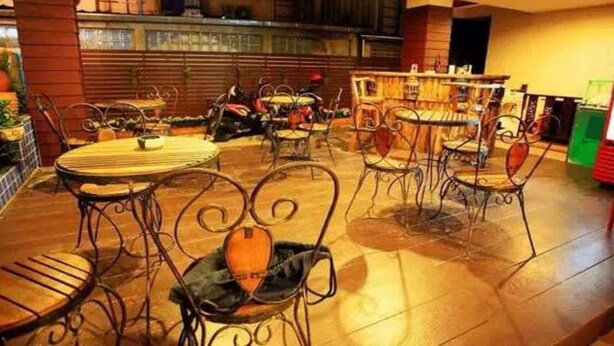 Un restaurante con mesas redondas y sillas de metal, una zona de bar y un suelo de baldosas.