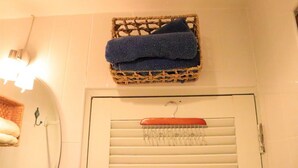 A bathroom with a wicker basket containing a folded towel, a wooden hanger with a towel, and a towel rack with a towel.