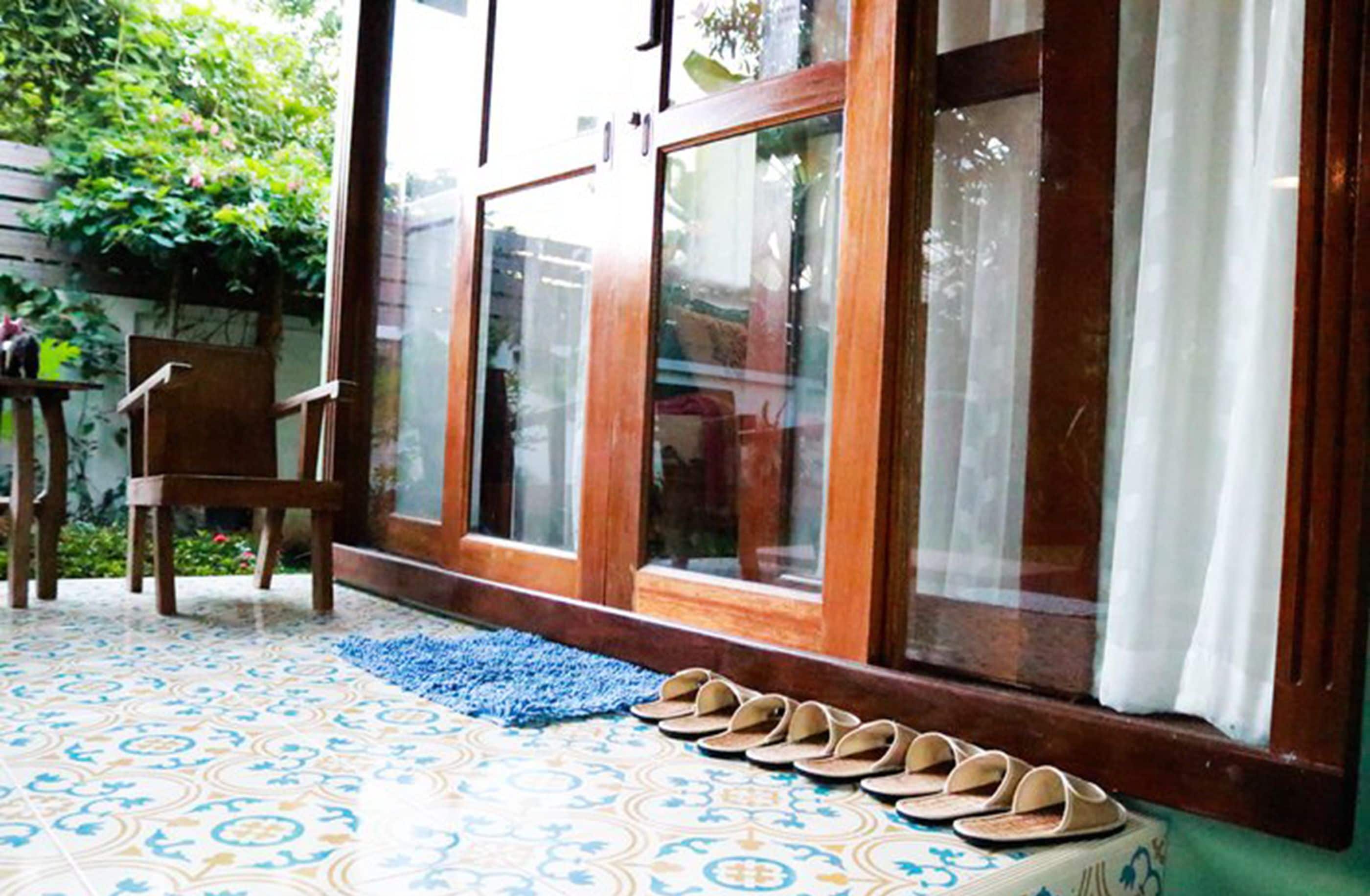 A room with a patterned floor, a wooden chair, and a row of sandals by a glass door with curtains.