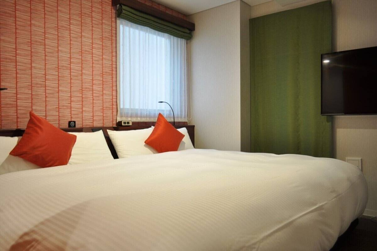 A hotel room with a large bed, two pillows, a flat-screen TV, and a window with curtains.