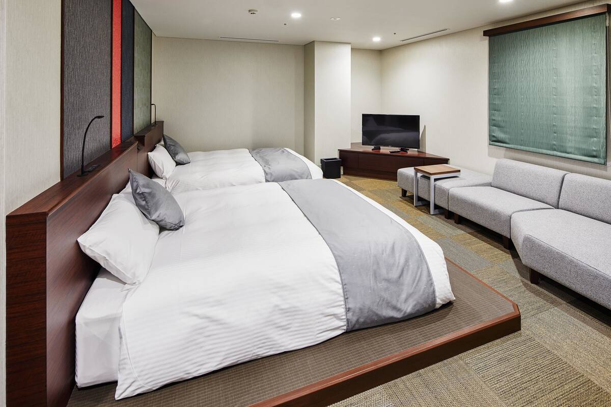 A hotel room with two beds, a sofa, a TV, and a large window.