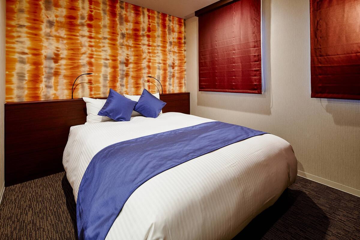A neatly made bed with a blue blanket and pillows, a wooden headboard, and a textured wall behind it.