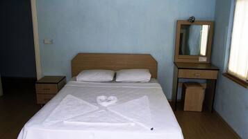 Una cama bien hecha con una toalla dispuesta en forma de corazón, una mesita de noche, un espejo y un equipo de aire acondicionado en la pared.