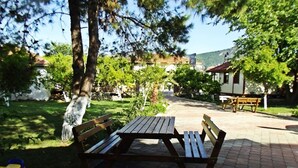 A picnic table with benches in a park area with trees and a building in the background. - Dalyan Gurkan Apart Hotel (Ortaca)