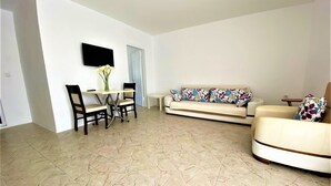 A living room with a sofa, a dining table with chairs, and a TV mounted on the wall. - Dalyan Gurkan Apart Hotel (Ortaca)