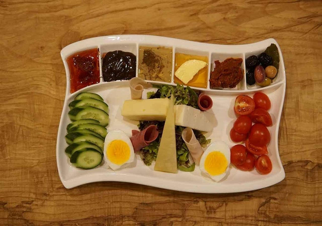 Un safata rectangular blanca amb diferents aliments, com trossos de pepino, ous, tomàquets i formatge.
