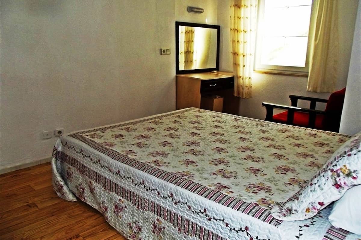 A bedroom with a bed, a bedside table, a mirror, and a window with curtains.