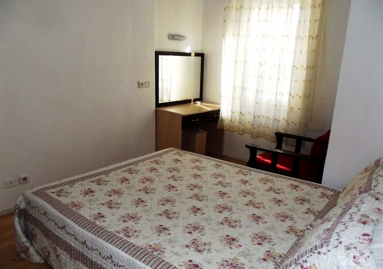 Un dormitorio con cama, mesita de noche, espejo y ventana con cortinas.