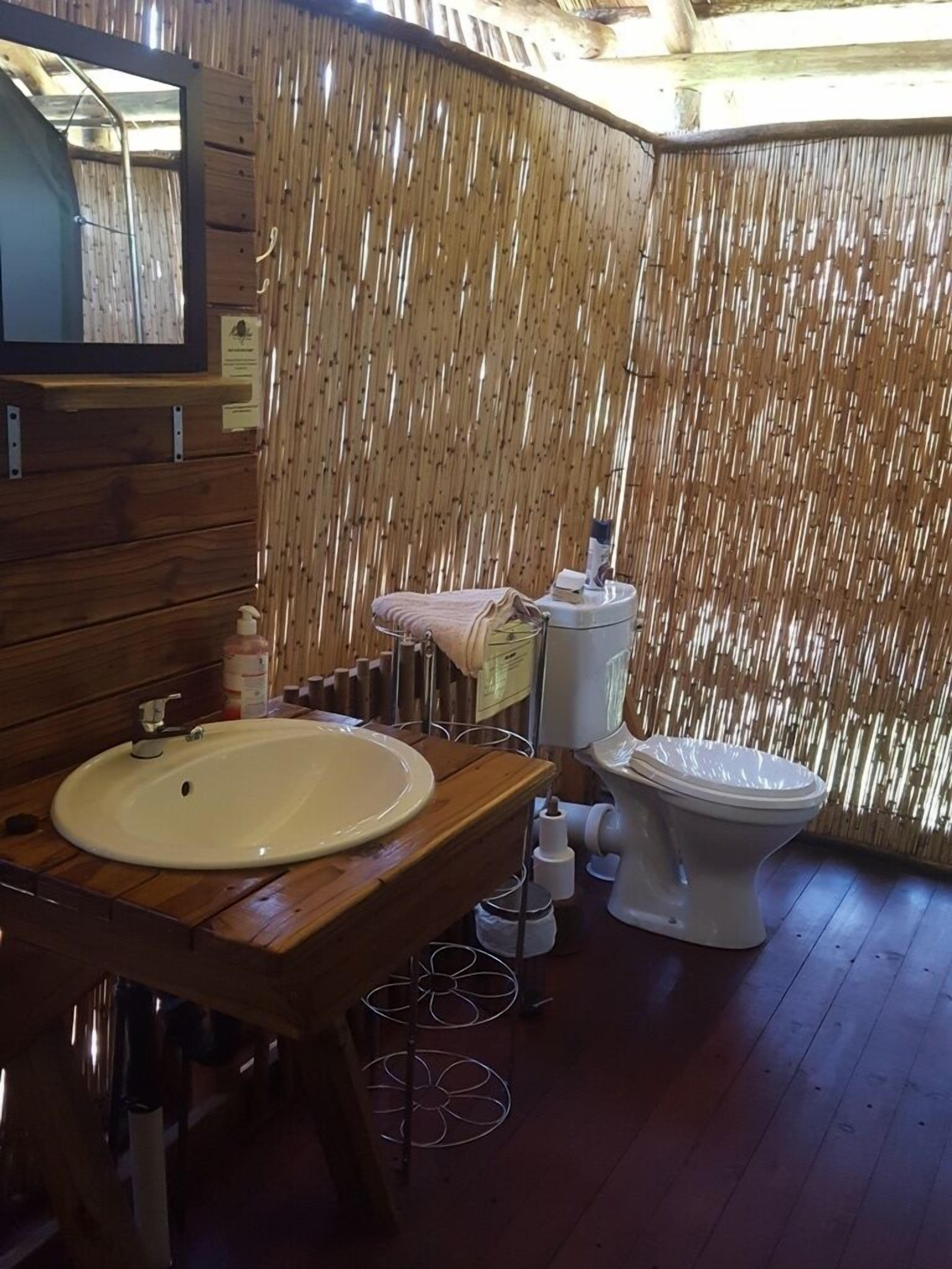 Un baño con tocador de madera, lavamanos, inodoro y pared de bambú.