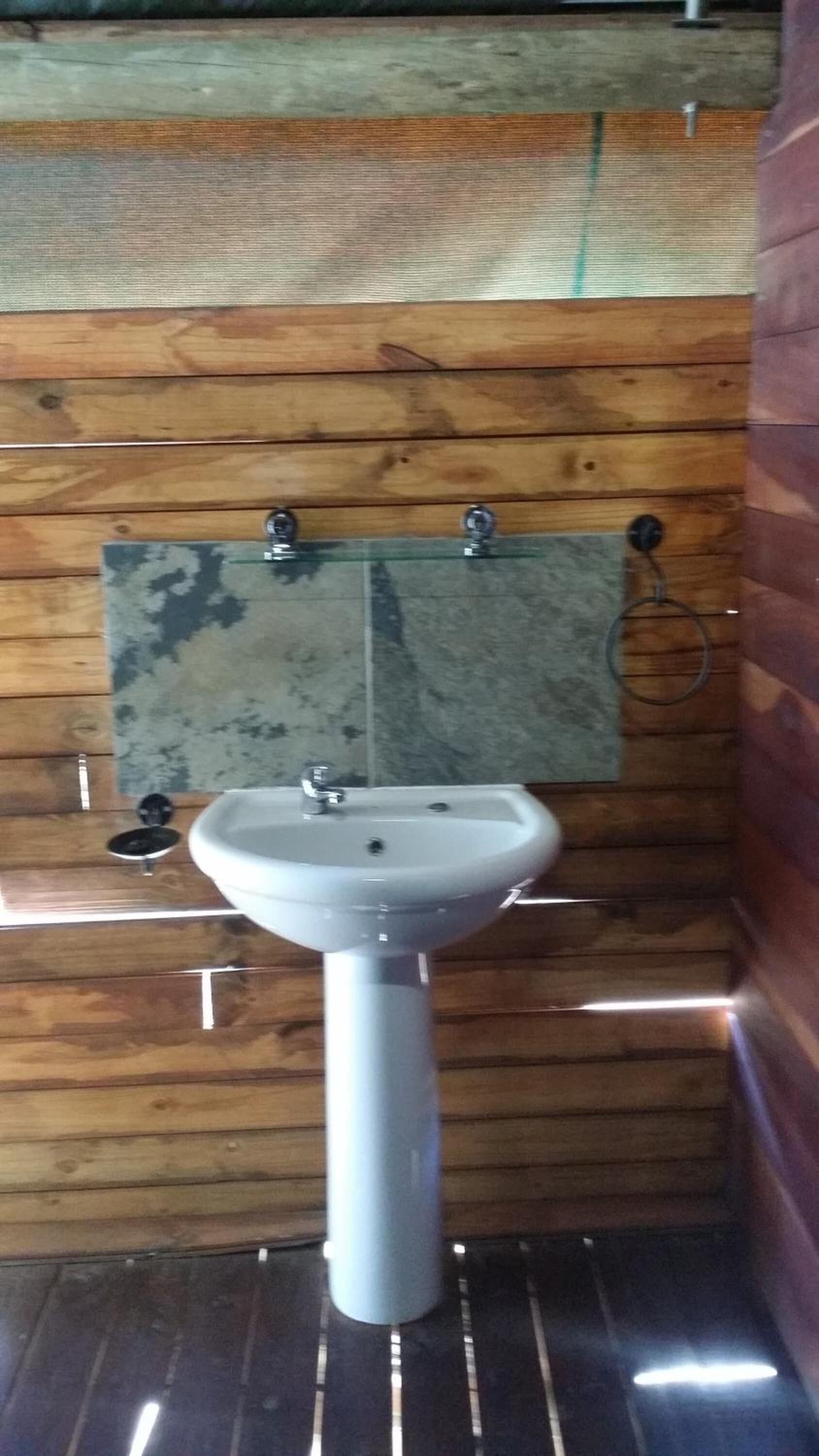 A bathroom with a white pedestal sink, wooden panel walls, and a tiled backsplash.