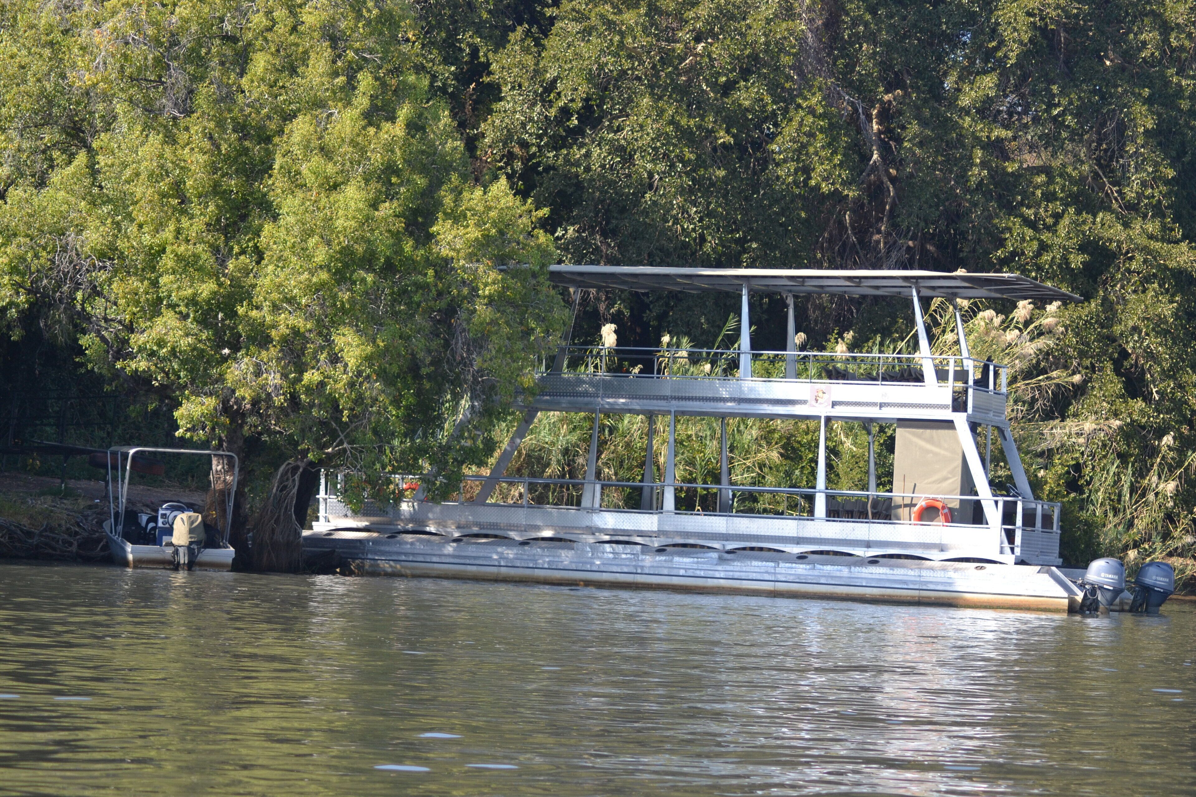 A houseboat with a covered upper deck, a lower deck with seating, and a motor at the stern.